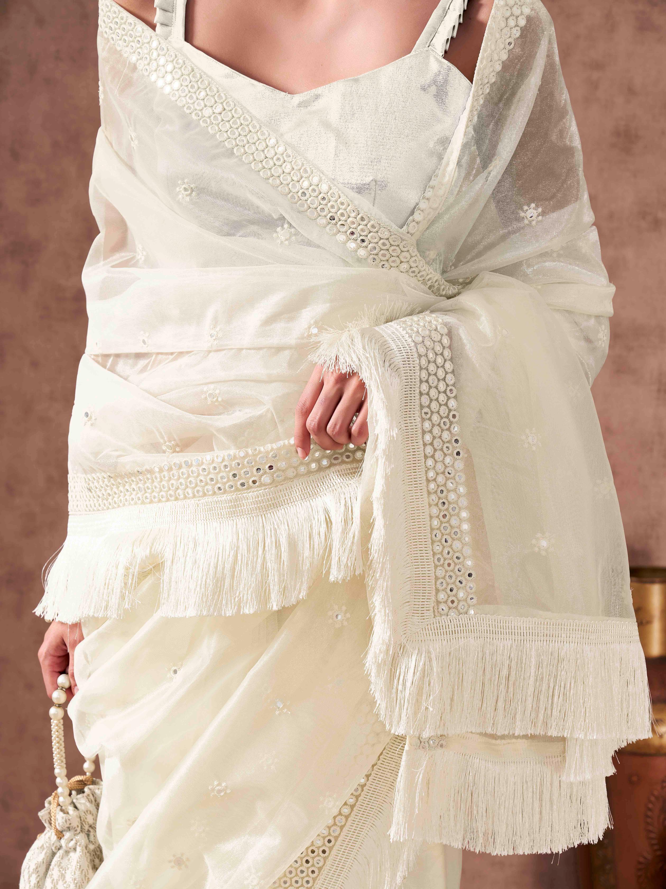 Off white colored supernet saree with faux mirror embroidery and tassles lace